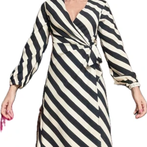 Randig omlottklänning - Snygg randig omlottklänning i svart och vit med långa ärmar. Klänningen har en v-ringad design och knytning i midjan för en smickrande passform. Perfekt för en stilren look.