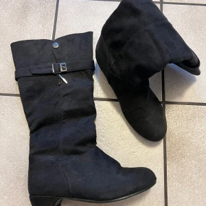 Svarta stövlar med leopardmönstrad insida - Snygga svarta stövlar med en leopardmönstrad insida. De har en dekorativ spänne och dragkedja på sidan. Perfekta för att ge en stilren look med en touch av vildhet.