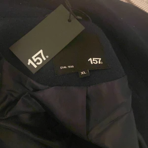 Marinblå kappa från lager 157 - Snygg marinblå kappa från 157 i storlek XL. Perfekt för kyligare dagar med sin klassiska design och dubbla knapprad. Ett stilrent val för den som gillar tidlös mode. Den är köpt igår inte använt den den var bara för stor på mig!!