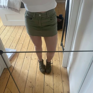 Olivgrön kortkjol - Snygg olivgrön kortkjol med fickor och knappdetaljer. Perfekt för en avslappnad stil. Kjolen har en klassisk design med en modern twist. I storlek 36 men skulle säga att den passar 32-36 då jag oftast har 32-34