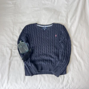 Svart stickad tröja från Ralph Lauren S - Ralph Lauren Cable Knit – Klassisk kabelstickad tröja i 100% bomull (eller annat material om det är relevant). Perfekt för en tidlös och stilren look. Diskret broderad logga på bröstet. Mjuk, bekväm och i fint skick. Passar både till vardags och mer uppklädda tillfällen. Ny pris ca 1800kr  ✔️ Skickas samma dag eller senast nästa! ✔️ Mätningar finns i bilderna.  Storlek S för 12-14 åringarHör av dig vid frågor!