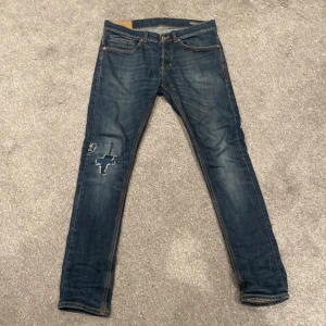 Blå jeans från Dondup - Snygga blå jeans från Dondup med slitna detaljer på ena benet. De har en klassisk femficksdesign och knappar i midjan. Perfekta för en avslappnad stil. Passar dig som är runt 175-185