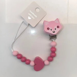 Napphållare med hjärta och räv - Handgjord napphållare i rosa nyanser med ett sött rävhuvud och hjärta. Perfekt för att hålla nappen nära och säker. Tillverkad med kärlek och omtanke. BPA pärlor, silikon och trä. 