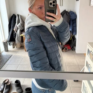 Vändbar dunjacka från Parajumpers - Säljer en vändbar dunjacka från Parajumpers i storlek S. Jackan har en stilren design med en sida i ljusgrå/silver och den andra i mörkblå. Den är quiltad och har dragkedja framtill. Perfekt för att variera din stil beroende på humör och väder.