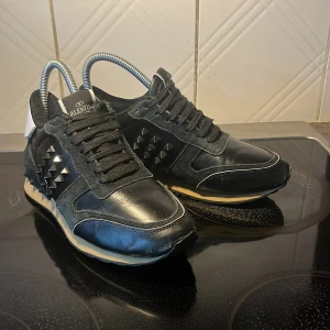 Svarta sneakers från Valentino - Snygga svarta Valentino sneakers med ikoniska nitar på sidorna och ett hjärtmotiv på hälen. Storlek 37,5 38,Skorna har en klassisk snörning och en bekväm sula. Bara att fråga om ni har funderingar 🙌