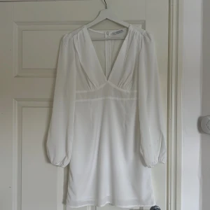 Vit klänning från Nelly x Glamorous - Säljer en elegant vit klänning från Nelly x Glamorous med v-ringad design och långa ärmar. Klänningen har en dragkedja i ryggen och är perfekt för en stilren look. Passar bra till både fest och andra speciella tillfällen som student och konfirmation🥰