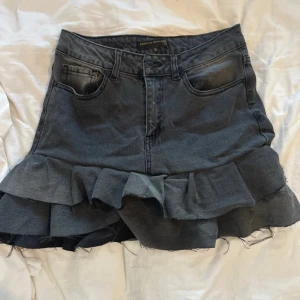 Svart jeanskjol från Pernilla Wahlgren - Trendig svart jeanskjol från Pernilla Wahlgren med volangdetaljer. Kjolen har en klassisk femficksdesign och en snygg tvättad look. Perfekt för att ge din outfit en cool touch. Sitter mer som en XS