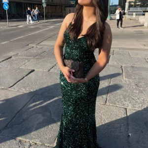 Grön paljett/ glitter bal klänning - En lång vacker mörk grön bal klänning. Jag köpte den i Paris förra året, pris kan diskuteras:) den är av paletter och glitter väldigt vackert. Klänningen är en XS. Klänningen är stretchig, mått på mig med korsett: Midja: 75,5cm Höft 99cm Längd från ryggens axelband eftersom den är längre bak än fram: 150cm (Jag är 160cm)
