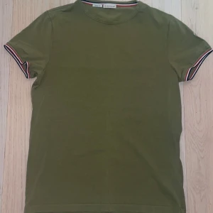 Grön t-shirt från Moncler - Säljer en grön t-shirt från Moncler i slim fit. T-shirten har ett litet nästan osynligt hål annars är den i bra skick. Pris kan diskuteras