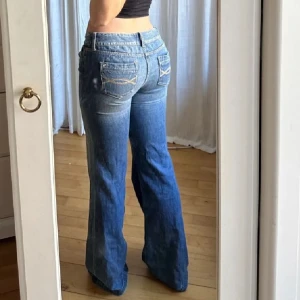 Blå jeans från Abercrombie & Fitch - Snygga blå jeans från Abercrombie & Fitch med bootcut-stil och låg midja. De har en klassisk femficksdesign och stängs med dragkedja och dubbla knappar. Perfekta för en avslappnad look.