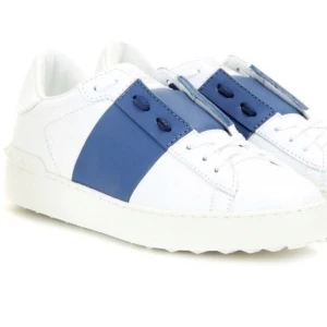 Valentino sneakers med blå detalj - Snygga vita Valentino sneakers med en bred blå rem över snörningen. Skorna har en klassisk design med rockstud-detaljer på hälen. Perfekta för en stilren look.