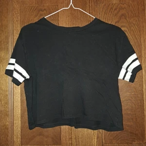 Svart kortärmad t-shirt från H&M - Säljer en svart croppad kortärmad t-shirt från H&M med vita ränder på ärmarna. 
