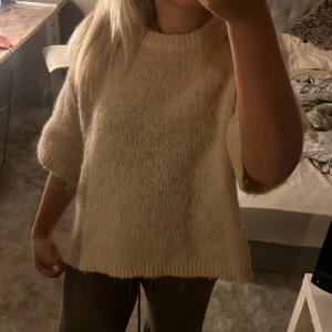 Beige stickad tröja från Aware - Mysig beige stickad tröja från Aware. Perfekt för kyliga dagar med sin mjuka och fluffiga textur. Tröjan har en rund hals och en avslappnad passform som ger en skön känsla. Ett måste för garderoben!