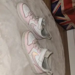 Snygga Nike sneakers i en kombination av rosa och vitt. Skorna har snörning och kardborreband för extra säker passform. Perfekta för en avslappnad stil med en touch av färg. Det är storlek 34 