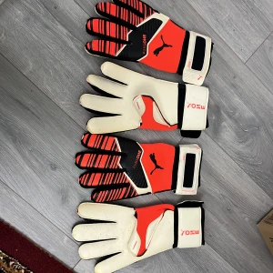 Puma One målvaktshandskar - Säljer ett par Puma One målvaktshandskar i rött och svart med vita detaljer. Handskarna har en justerbar handledsrem för bättre passform och grepp. Perfekta för fotbollsmatcher och träning. Handskarna är helt nya 