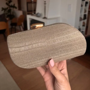 Guldig kuvertväska från True Decadence - Snygg guldig kuvertväska från True Decadence med en elegant guldfärgad låsdetalj. Väskan har en stilren design och en kedja för att bära den över axeln. Perfekt till ett festligt tillfälle ex bal.