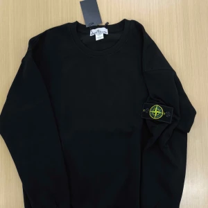 Svart tröja från Stone Island - (Pris kan gå ner vid snabbäffar)Säljer en stilren svart tröja från Stone Island med deras ikoniska märke på ärmen. Tröjan har en rund halsringning och långa ärmar, perfekt för en casual look. Passar bra till både jeans och chinos.
