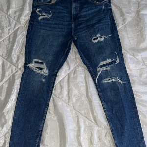 Blå jeans från Bershka - Snygga blå jeans från Bershka med slitna detaljer på framsidan. De har en modern passform och är perfekta för en avslappnad stil. Tillverkade i denim med en klassisk femficksdesign.