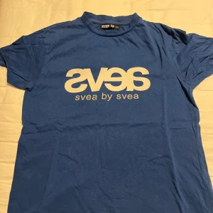 Blå t-shirt från Svea - Säljer en blå t-shirt från Svea med tryck på framsidan. T-shirten har en klassisk rund hals och korta ärmar. Perfekt för en avslappnad stil. 💙