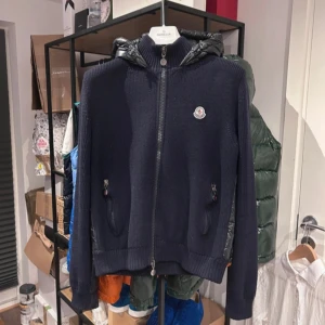 Mörkblå stickad jacka från Moncler - Säljer en snygg mörkblå stickad jacka från Moncler med dragkedja och huva. Jackan har Moncler-loggan på bröstet och ribbade muddar. Perfekt för kyliga dagar! byten tillgängliga💫🙌