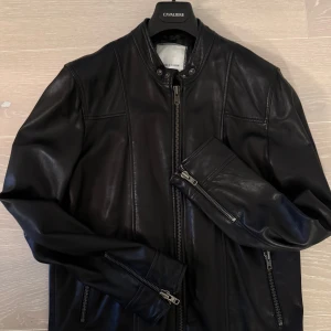 Svart mjuk skinnjacka från Samsøe Samsøe -Medium - Snygg svart skinnjacka från Samsøe Samsøe i modellen Krede. Jackan har en stilren design med dragkedja och tryckknappar vid kragen. Perfekt för en cool och avslappnad stil. Använt få gånger. Nypris: 5990kr