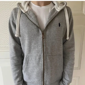 Grå hoodie från Ralph Lauren - Säljer en stilren grå hoodie från Ralph Lauren med dragkedja och justerbar huva. Mycket bra skick och pris kan diskuteras