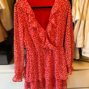 Röd blommig klänning från H&M Divided - Säljer en röd blommig klänning från H&M Divided med volangdetaljer och omlott-design