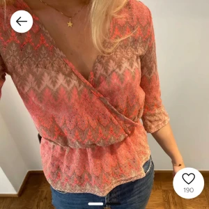 Mönstrad omlottblus i rosa och beige - Säljer en snygg omlottblus i rosa och beige med ett zigzag-mönster. Blusen har trekvartsärmar och en v-ringad design som ger en elegant look. Perfekt för både vardag och festliga tillfällen.