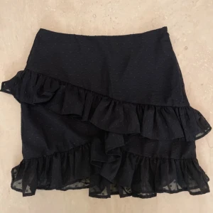 Svart kjol med volanger från Bik Bok - Supersöt svart kjol från Bik Bok med volanger. Kjolen har en dragkedja på sidan och ”prickigt” tyg. Som oanvänd!