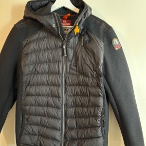 Parajumpers Nolan - Snygg svart jacka från Parajumpers med quiltad framsida och huva. Jackan har dragkedja och en liten bröstficka. Perfekt för kyligare dagar.