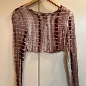 Brun- och vitrandig croppad topp - Säljer en brun- och vitrandig croppad topp med långa ärmar. Toppen har ett unikt mönster och är perfekt för en trendig look. Den är tillverkad i ett mjukt och bekvämt material. Med byxorna.