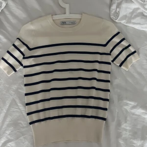 Randig tröja från Zara - Säljer en stilren randig tröja från Zara i beige och svart. Tröjan har korta ärmar och en klassisk rund halsringning. Perfekt för en avslappnad look.