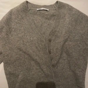 Grå kofta från Zara - Mysig grå kofta från Zara med v-ringning och knappar framtill. Perfekt för kyliga dagar med sin mjuka och bekväma passform. Priset kan diksuteras
