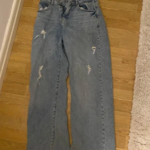 Blå jeans med slitningar  - Snygga blå jeans med slitningar på låren och knäna. De har en hög midja och en avslappnad passform.  Waist 26 - length 30. Knappt använda