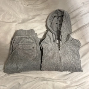 Juicy Couture ljus grå sätt - Säljer en Juicy Couture grå hoodie med dragkedja och huva. Perfekt för en avslappnad stil. Den har långa ärmar och ribbade muddar. Matchande byxor med fickor ingår.