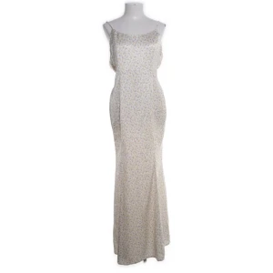 Blommig långklänning från NA-KD - Säljer en elegant långklänning från NA-KD med ett blommigt mönster i lila och orange på en vit bakgrund. Klänningen har en öppen rygg och smala axelband, perfekt för sommarens fester. Tillverkad i polyester för en lätt och bekväm känsla.