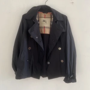 BURBERRY TRENCHCOAT - kort kappa/trenchcoat från Burberry. strl L/M. Köpt sekundhand för liknande pris, men har ingen garanti för äkthet. En sömn som är tidigare lagad, men inga andra defekter! 