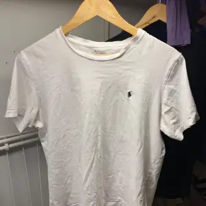 Säljer en klassisk vit t-shirt från Ralph Lauren med den ikoniska loggan broderad i blått på bröstet. T-shirten är kortärmad och tillverkad i mjuk bomull. Perfekt för en stilren look.