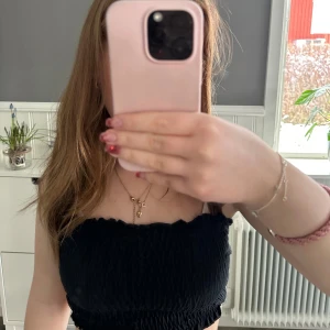 Svart tubtopp - Säljer en svart tubtopp med smockad design. Perfekt för varma dagar eller som ett lager under en jacka. Enkel och mångsidig topp som passar till det mesta. 