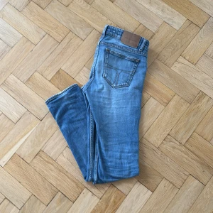 jeans från Tiger of Sweden - Snygga blå jeans från Tiger of Sweden med klassisk femficksdesign och knappgylf. Perfekta för en stilren look. Märkeslappen syns tydligt på insidan av midjan.