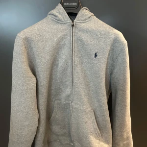 Grå hoodie från Ralph Lauren Strl 170 - Säljer denna sjukt fräscha zip hoodie från Ralph Lauren. Säljes pga att jag använt den ytterst få gånger och därmed är tröjan i nyskick. Hör gärna av er vid funderingar! 
