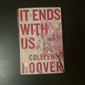 It Ends With Us - Säljer boken 'It Ends With Us' av Colleen Hoover. Omslaget är i rosa och beige med blommönster. Perfekt för dig som älskar romantiska och känslosamma berättelser. En populär bok som har fått mycket uppmärksamhet.