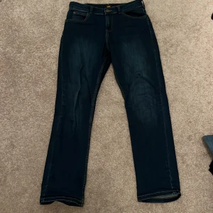 Lee Jeans - Snygga mörkblå jeans från Lee med klassisk femficksdesign och knappgylf. Perfekta för en stilren look. Märkeslogga på baksidan av midjan.