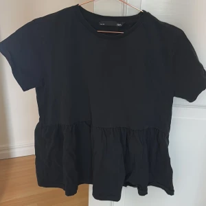 Svart topp från 157 - Säljer en svart topp från 157 i storlek S. Toppen har korta ärmar och en volangdetalj nedtill som ger en fin touch. Perfekt för en avslappnad stil.