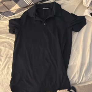 Svart pikétröja från Cutter & Buck - Säljer en stilren svart pikétröja från Cutter & Buck. Tröjan har korta ärmar och en klassisk krage med knappar. Perfekt för en avslappnad men ändå snygg look. Passar bra till både jeans och chinos. Storlek S men passar även M