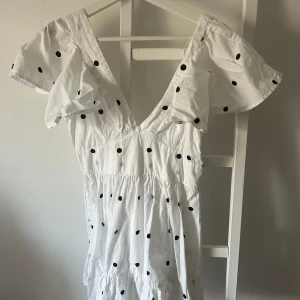 Vit prickig klänning från Gina Tricot - Söt vit klänning med svarta prickar från Gina Tricot. Den har korta ärmar med volangdetaljer och en v-ringad design. Perfekt nu i sommar!💗💗