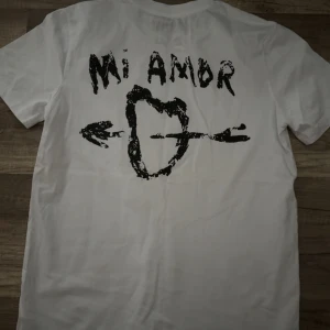 Mira Paris Mi Amor t-shirt - Säljer en vit t-shirt med ett coolt tryck på baksidan som säger 'Mi Amor' och har en pil genom ett hjärta. Perfekt för en avslappnad stil.