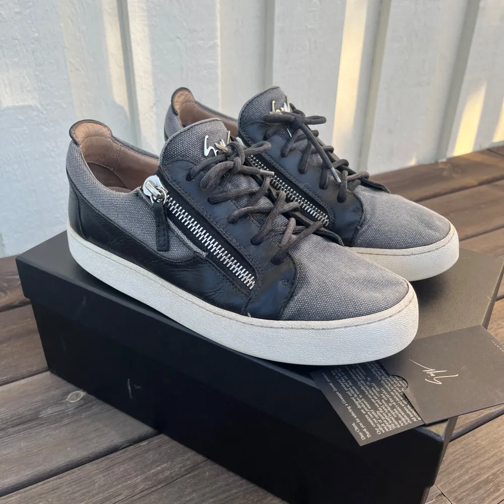 Snygga sneakers från Giuseppe Zanotti i grått och svart med coola dragkedjor på sidorna. Skorna har en rund tå och snörning, vilket ger en modern look. Nypris på dessa ligger på ca 3800kr. Medföljer OG box. Skorna är i bra skick.. Kengät.