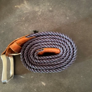 Flätat bälte från Jack & Jones - Snyggt flätat bälte i mörkblått med bruna läderdetaljer från Jack & Jones. Perfekt för att ge en stilren touch till din outfit. Spännet är i silverfärgad metall.