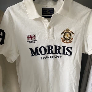 Vit pikétröja från Morris Gents - Säljer en stilren vit pikétröja från Morris Gents med broderade detaljer och en klassisk krage. Storlek S